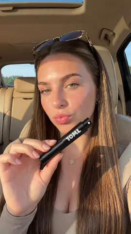 A woman in a sunlit car holding up a black 10ML atomiser
